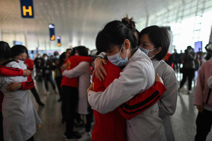 TOPSHOT - Medical staff from Jilin Province (in red) hug nurses from Wuhan after working together during the COVID-19 coronavirus outbreak during a ceremony before leaving as Tianhe Airport is reopened in Wuhan in China's central Hubei province on April 8, 2020. - Thousands of Chinese travellers rushed to leave COVID-19 coronavirus-ravaged Wuhan on April 8 as authorities lifted a more than two-month prohibition on outbound travel from the city where the global pandemic first emerged. (Photo by Hector RETAMAL / AFP)
