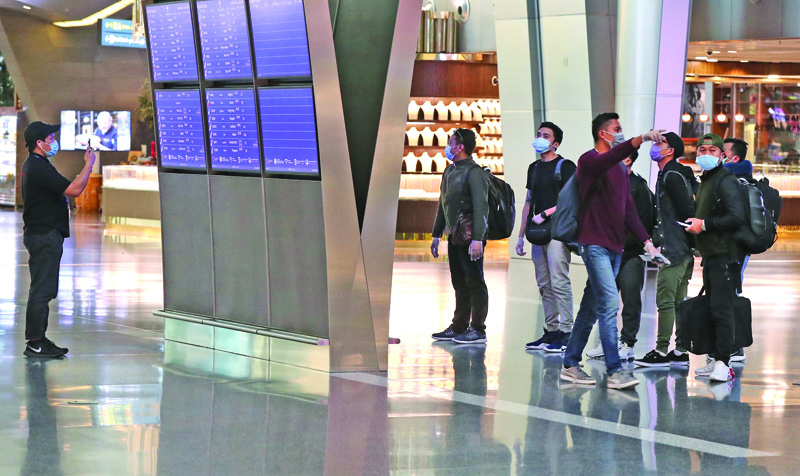 (FILES) In this file photo taken on April 01, 2020, travellers wearing face masks due to the COVID-19 coronavirus pandemic, check their flights on information displays at Hamad International Airport in the Qatari capital Doha. - Qatar has seen its airline's crews applauded and won thumbs-up from governments after repatriating thousands of travellers stranded by the coronavirus aviation shutdown. Observers say Doha is hoping that by keeping its planes in the skies, in contrast to its regional competitors, it will win diplomatic points (Photo by KARIM JAAFAR / AFP)