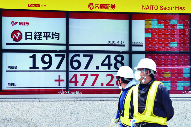 Pedestrians walk past a quotation board displaying share prices of the Tokyo Stock Exchange in Tokyo on April 17, 2020. - Tokyo's benchmark Nikkei index rallied more than 3.1 percent on April 17 as investors welcomed a pledge by President Donald Trump to press ahead with reopening the US economy. (Photo by Kazuhiro NOGI / AFP)