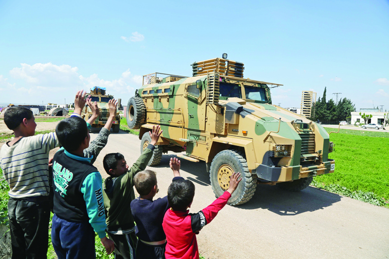 Syrian youths wave to a convoy of Turkish military reinforcements advancing near the town of Hazano in the countryside of Syria's Idlib province, on April 12, 2020, on the highway linking the Bab al-Hawa border crossing with Turkey to Idlib. (Photo by Aref TAMMAWI / AFP)