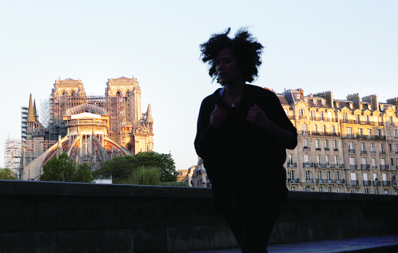 A jogger runs on a empty boulevard past the Paris' Cathedral Notre Dame at the sunrise on the eve of the first anniversary of the violent fire who destroyed a large part of the monument, on April 14, 2020, on the twenty-nineth day of a lockdown in France to stop the spread of the  COVID-19, (the novel coronavirus). - One year ago, on April 15, 2019, a fire erupted in Notre-Dame Cathedral in Paris, partly destroying the nearly millenium old building and its precious artworks visited by millions of people a year. (Photo by THOMAS COEX / AFP)