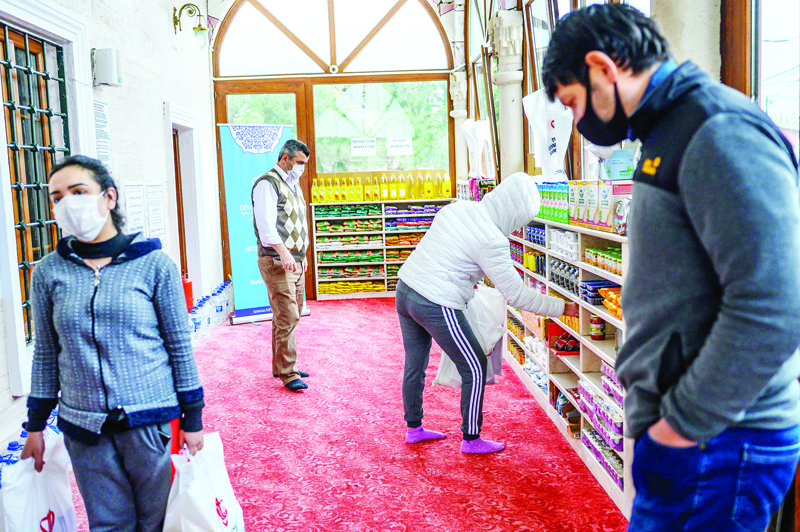 People take their need on April 21, 2020, in the Sariyer district of Istanbul, at the entrance of the Dedeman mosque where the racks reserved for shoes of the Muslim faithful is instead loaded with food which reminds one of a supermarket but they are destined for the needy hard hit by the coronavirus pandemic, after Turkey suspended mass prayers in mosques until the risk of COVID-19 outbreak passes. (Photo by Bulent Kilic / AFP)
