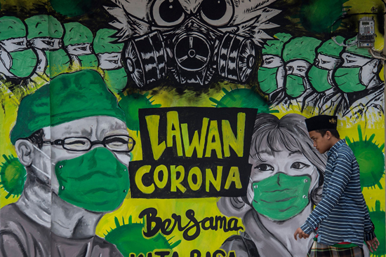 TOPSHOT - A man walks past a mural depicting the COVID-19 coronavirus in Surabaya on April 6, 2020. (Photo by Juni Kriswanto / AFP)