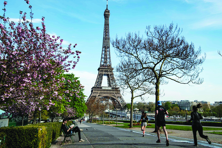 This picture taken on April 7, 2020 shows runners at the closed Jardin du Champs de Mars garden in front of the Eiffel tower in Paris, on the 22nd day of a lockdown in France aimed at curbing the spread of the COVID-19 pandemic, caused by the novel coronavirus. (Photo by BERTRAND GUAY / AFP)