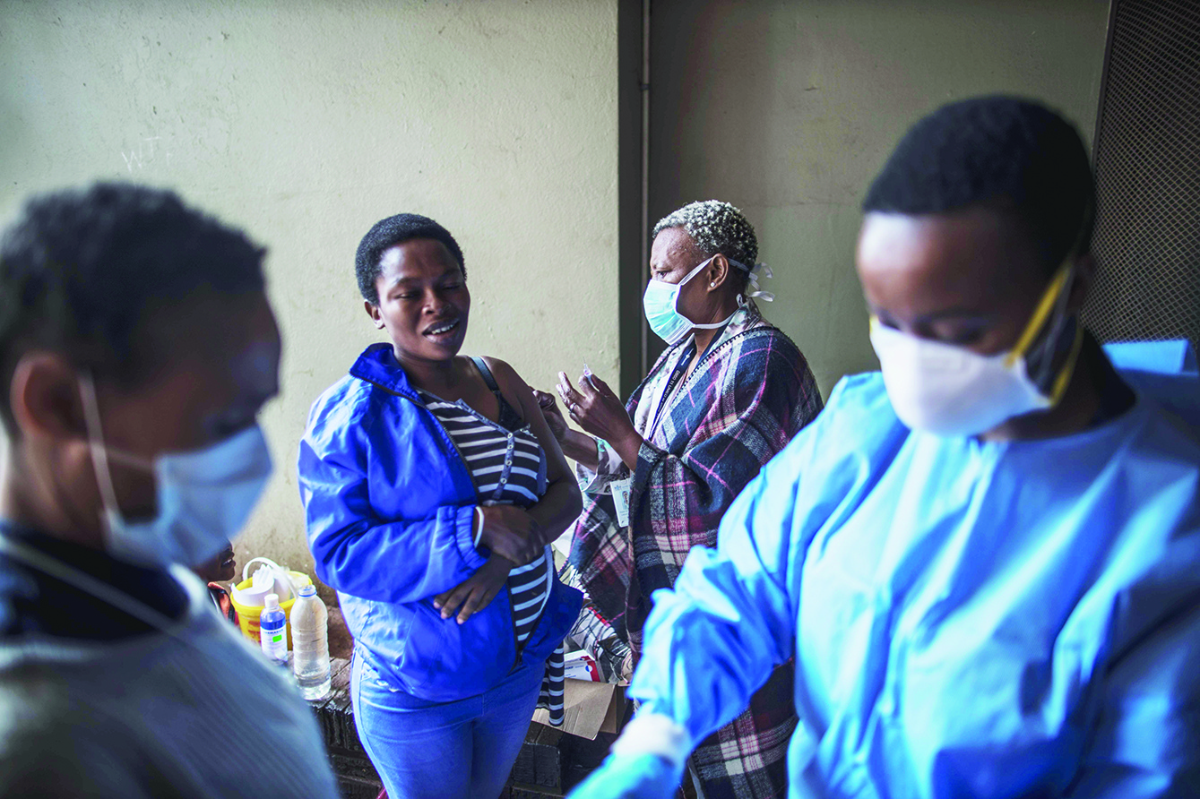A woman reacts as she receives a flue vaccine while a Gauteng Health Department Official gets ready before collecting samples during a door-to-door COVID-19 coronavirus testing drive in Yeoville, Johannesburg, on April 3, 2020. (Photo by MARCO LONGARI / AFP)