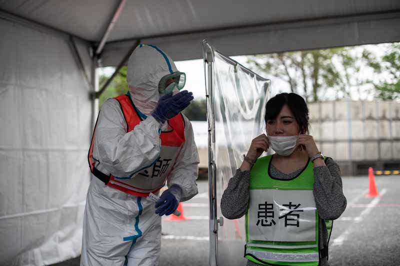 A doctor (L-in orange vest) in protective clothing and an official (R) playing the role of a patient take part in a demonstration of a drive-through polymerase chain reaction (PCR) swab test for the COVID-19 coronavirus in Fujisawa in Kanagawa prefecture, southwest of Tokyo, on April 27, 2020. (Photo by Philip FONG / AFP)