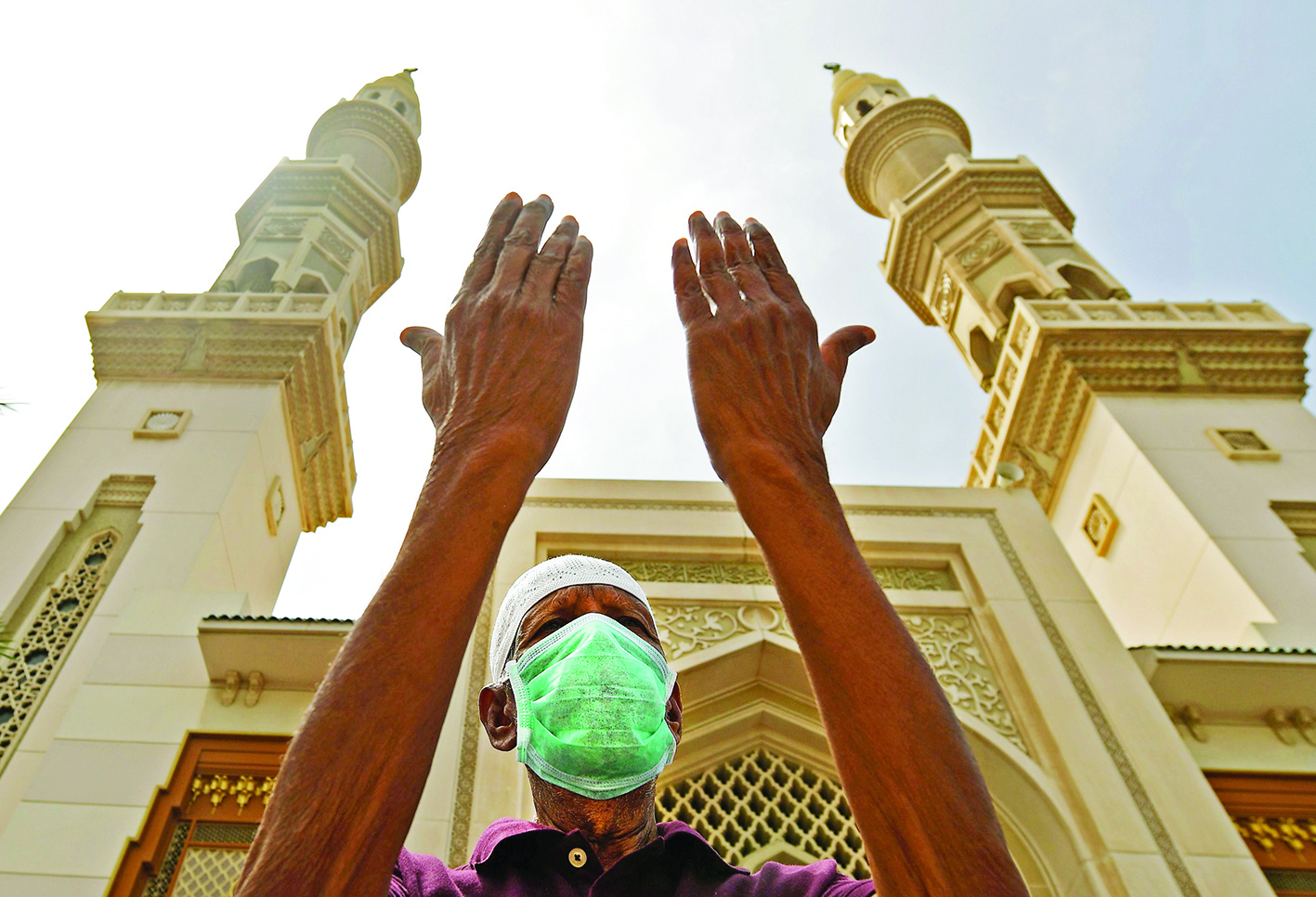 An elderly man wearing a protective mask lifts his hands in prayer outside a mosque which has been closed to worshipers amid the COVID-19 coronavirus pandemic, in Sharjah, in the United Arab Emirates, on March 30, 2020. (Photo by KARIM SAHIB / AFP)
