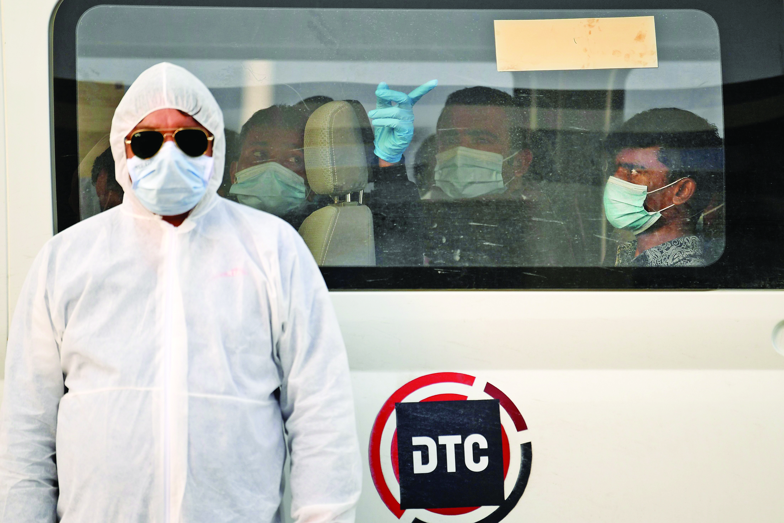 A health worker stands in front of a bus driving migrant workers who have been tested positive for the COVID-19 to the Warsan neighbourhood, where people infected or suspected of being infected by the virus are quarantined, in the Gulf Emirate of Dubai, on April 22, 2020. (Photo by KARIM SAHIB / AFP)