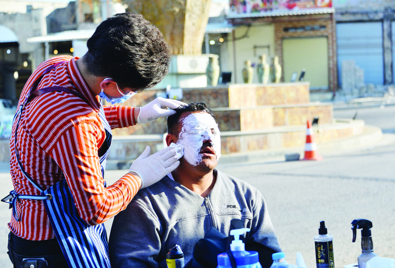 TOPSHOT - An Iraqi hairdresser, wearing personal protective equipment, provides a facial mask to a member of the security forces during the coronavirus (COVID-19) pandemic in the northern Iraqi city of Mosul on April 18, 2020. (Photo by Zaid AL-OBEIDI / AFP)