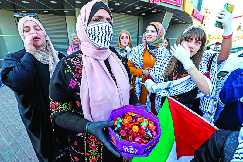 Family members of 18-year-old Palestinian Amir Naji, released by Israel from prison, hand out chocolates and celebrate ahead of his arrival while clad in latex gloves and face masks due to the COVID-19 coronavirus pandemic, at a checkpoint near the city of Ramallah in the occupied West Bank on April 14, 2020. - When Palestinian Amir Naji was released from Israeli prison he was told not to hug his family, but emotion overwhelmed him and he clutched his mother tight before his father him away, before being hurried to a nearby hotel for two weeks of isolation alongside other released prisoners. Israel's response to the coronavirus pandemic has included efforts to prevent outbreaks in prisons, including regular sterilisation, checking temperatures of staff daily, and stopping visits from family and lawyers. But advocates are calling for more -- urging the Jewish state to release at-risk prisoners. (Photo by ABBAS MOMANI / AFP)