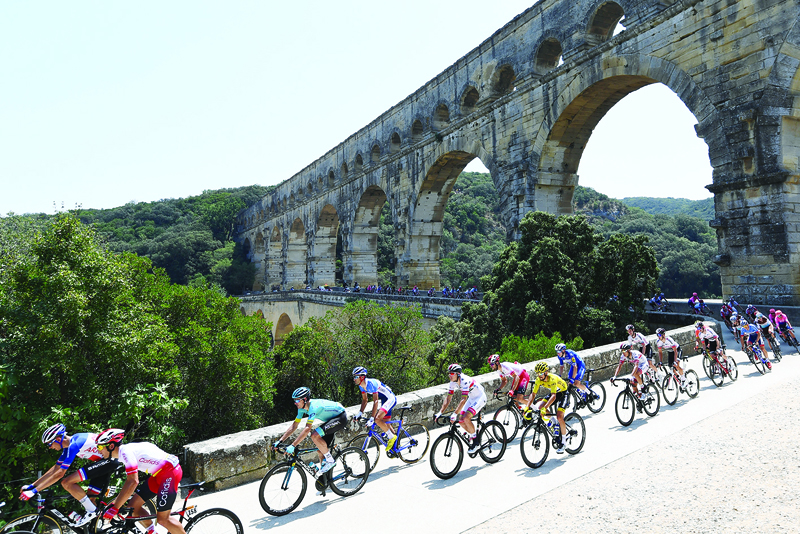 (FILES) In this file photo taken on July 23, 2019 France's Julian Alaphilippe (frontC), wearing the overall leader's yellow jersey and cyclists cross the Pont du Gard during the sixteenth stage of the 106th edition of the Tour de France cycling race between Nimes and Nimes, in Nimes. - The Tour de France is not only a French monument, but also the economic heartbeat of professional cycling itself and analysts fear heavy consequences if the coronavirus crisis forces its cancellation. An announcement is expected this week on either a postponement or an outright cancellation of the 21-day extravaganza that is currently scheduled to start in Nice on June 27. (Photo by Anne-Christine POUJOULAT / AFP)