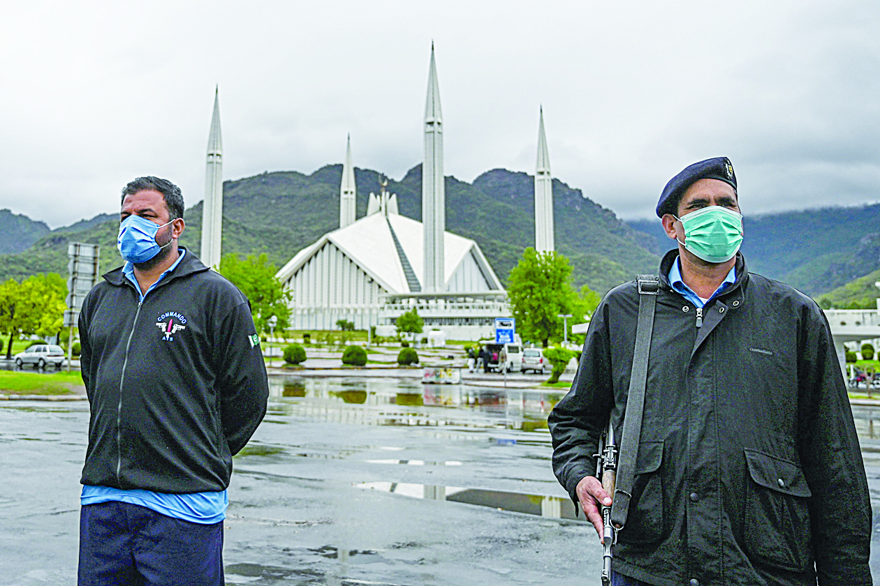 Policemen wearing facemasks stand guard at a checkpoint beside the Grand Faisal Mosque during a government-imposed nationwide lockdown as a preventive measure against the COVID-19 coronavirus, in Islamabad on March 27, 2020. (Photo by Aamir QURESHI / AFP)