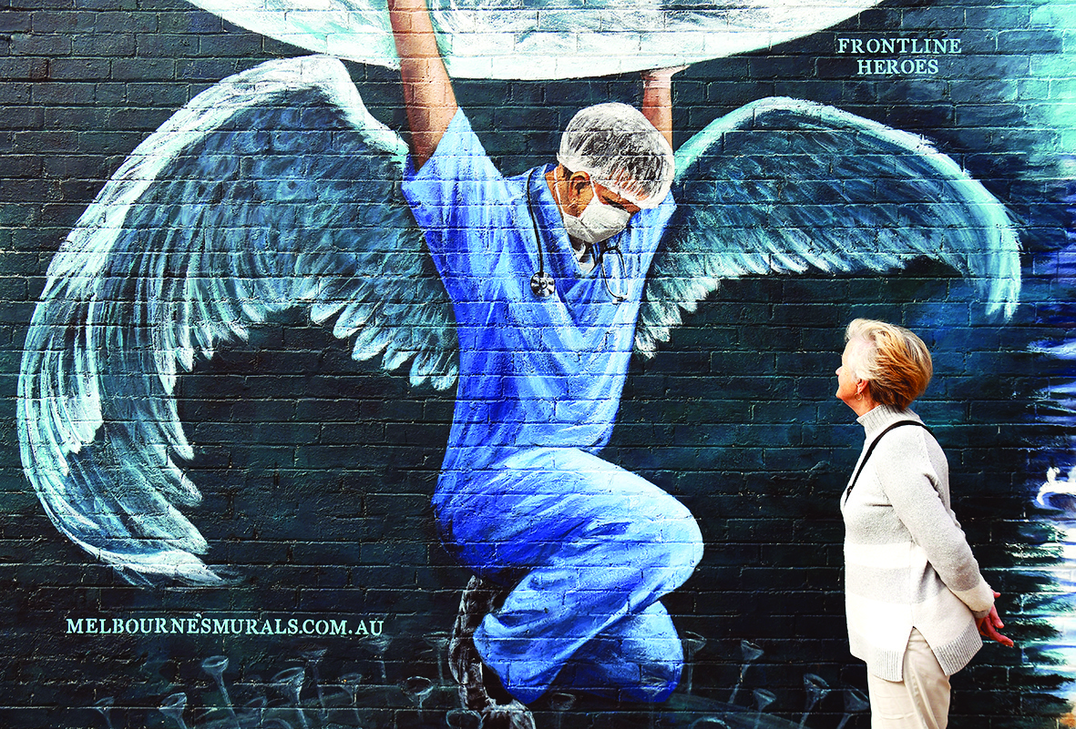 A woman looks at a mural of a health worker with wings holding a globe on International Nurses Day in Melbourne on May 12, 2020. - As frontline hospital staff are constantly facing the risks from the COVID-19 coronavirus outbreak, the world is marking International Nurses Day, celebrated around the world every May 12, the anniversary of Florence Nightingale's birth. (Photo by William WEST / AFP)
