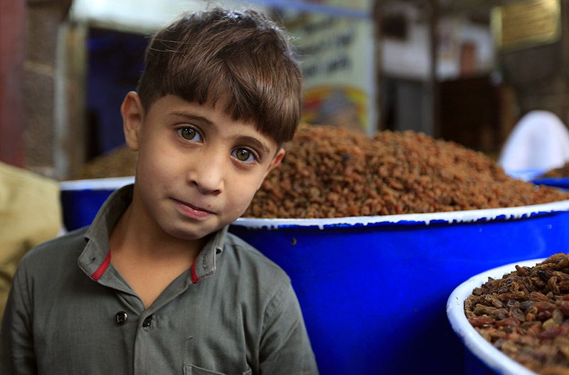 A boy stands before barrels of raisins at an open-air market in Yemen's capital Sanaa on May 20, 2020, as Muslims shop ahead of the Eid al-Fitr holiday marking the end of the holy fasting month of Ramadan. (Photo by Mohammed HUWAIS / AFP)