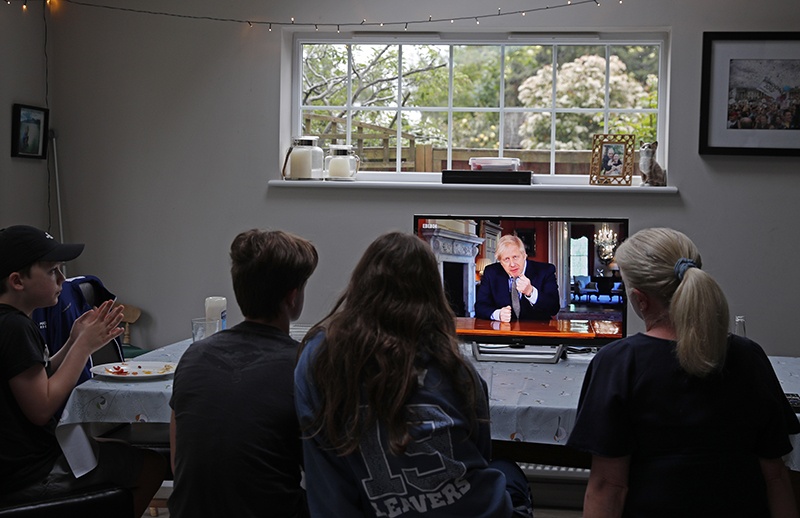 A family gather around the television to watch Britain's Prime Minister Boris Johnson give a televised message to the nation in Hartley Wintney, west of London on May 10, 2020, as the government sets out it's roadmap to ease the national lockdown due to the novel coronavirus COVID-19 pandemic. - Prime Minister Boris Johnson issued new stay-at-home advice on Sunday and warned he would proceed cautiously on lifting a nationwide coronavirus lockdown as the death toll in Britain, already the highest in Europe, continues to mount. (Photo by Adrian DENNIS / AFP)