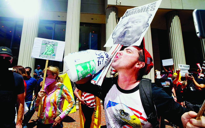TOPSHOT - A demonstrator holding an anti-Trump sign, pretends to drink from a bottle of bleach during a rally to re-open California and against Stay-At-Home directives on May 1, 2020 in San Diego, California. - Rallies have been held at several state capitols across the country as protesters express their deep frustration with the stay-at-home orders that are meant to stem the spread of the novel coronavirus. (Photo by Sandy Huffaker / AFP)