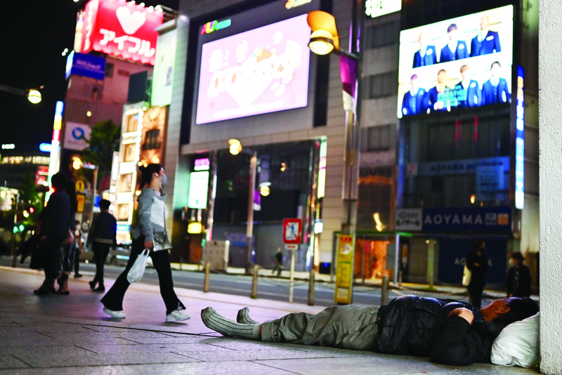 A woman wearing a facemask amid concerns over the spread of the COVID-19 coronavirus wals past a man laying on the street in Tokyo on May 4, 2020. - Japan's Prime Minister Shinzo Abe on May 4 extended a state of emergency over the coronavirus until the end of May, as the government warned it was too soon to lift restrictions. (Photo by CHARLY TRIBALLEAU / AFP)
