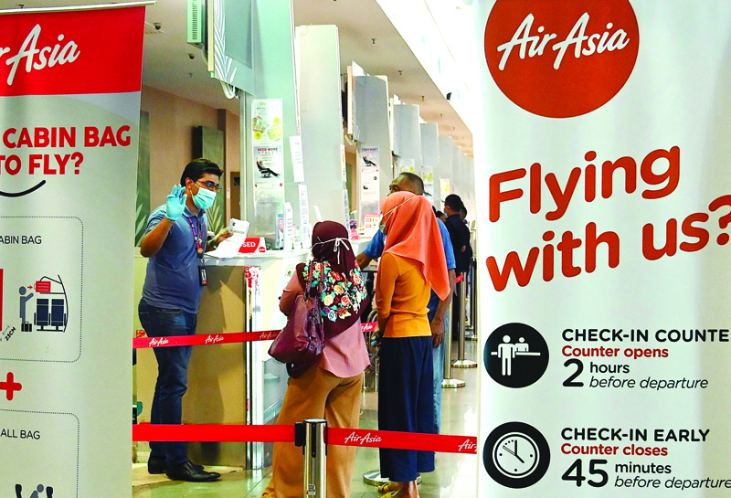 Passengers speak to a worker wearing a protective face mask and gloves as they check in for a flight at Penang International Airport as AirAsia resumed domestic flights in Malaysia, in Penang on April 29, 2020, after the airline's operations were curtailed due to the spread of the COVID-19 coronavirus. (Photo by GOH CHAI HIN / AFP)