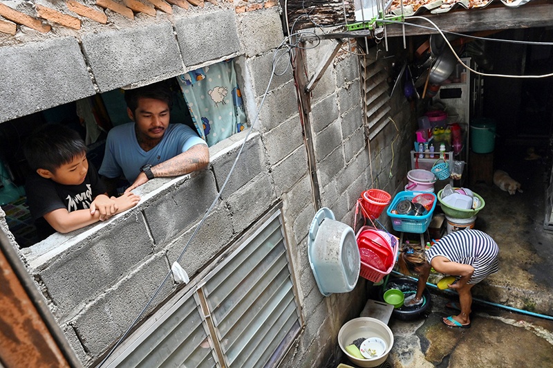 This photo taken on May 30, 2020 shows motorcycle taxi driver, Thanapat Noidee with son Kittipat looking from the window of their home in Bangkok. - Shuffling around their tiny slum home which is too small to stand up in, a couple share donated noodles with their sons and worry about how they will pay the bills, as the coronavirus pushes Thailand's poor deeper into penury. (Photo by Romeo GACAD / AFP) / TO GO WITH Health-virus-Thailand-economy-poverty by Pitcha DANGPRASITH