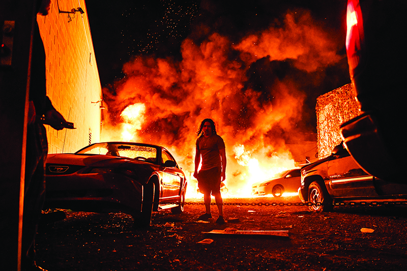 MINNEAPOLIS: A man tries to tow away a car in a safe zone as another car catches fire in a local parking garage on Friday during a protest over the death of an unarmed black man. — AFP