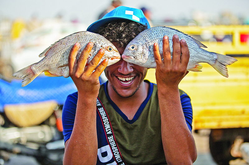 AL-FAW: A youth poses while holding two fish before his face in Iraq’s southern port city of Al-Faw, 90 kilometers south of Basra near the Shatt al-Arab and the Gulf. — AFP