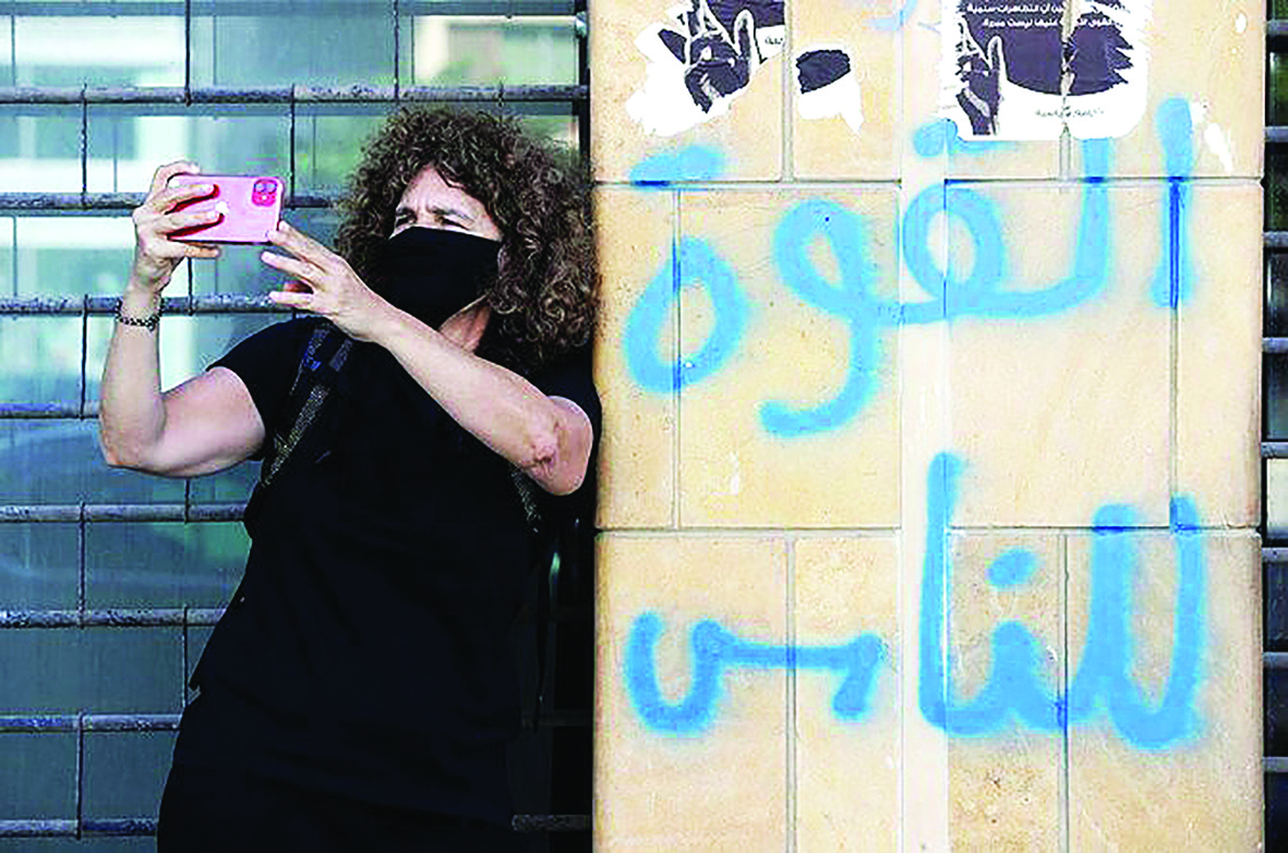 Lebanese director Carol Mansour uses her phone to film while wearing a face mask and standing by graffiti reading in Arabic “power to the people”, in Beirut. –AFP