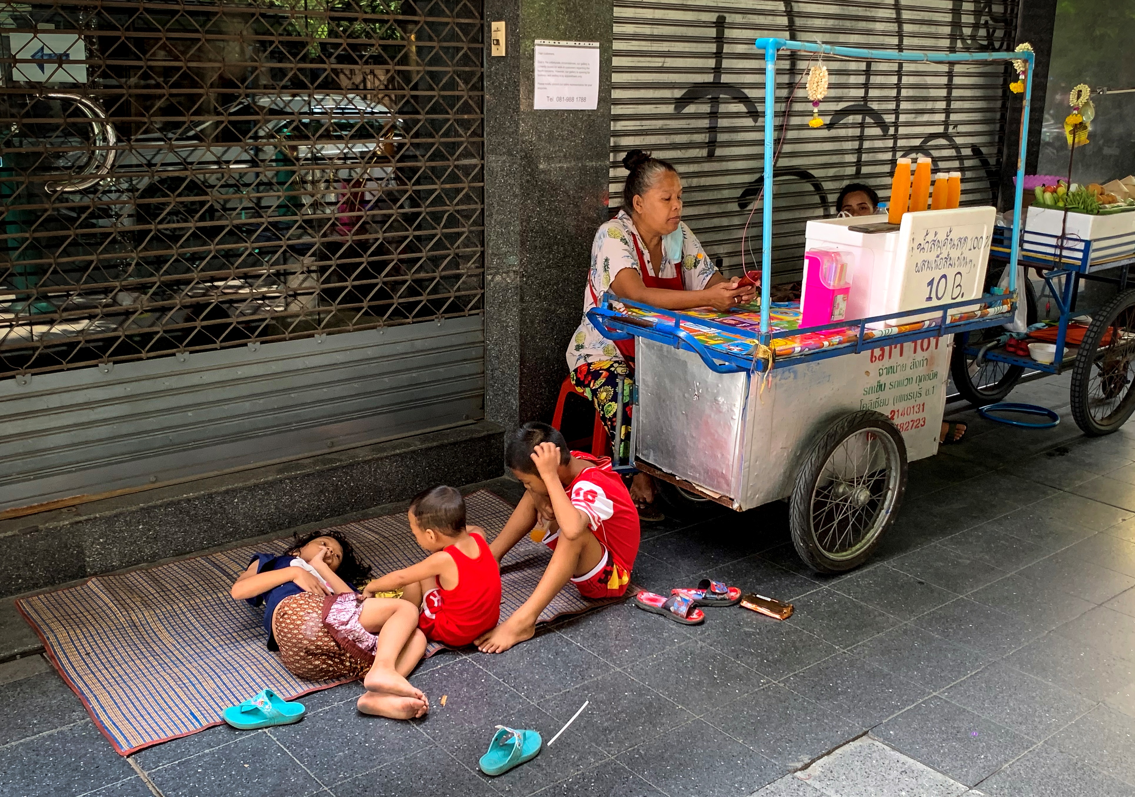 The children of a fruit juice vendor play next to her cart in Bangkok on June 25, 2020. (Photo by Mladen ANTONOV / AFP)