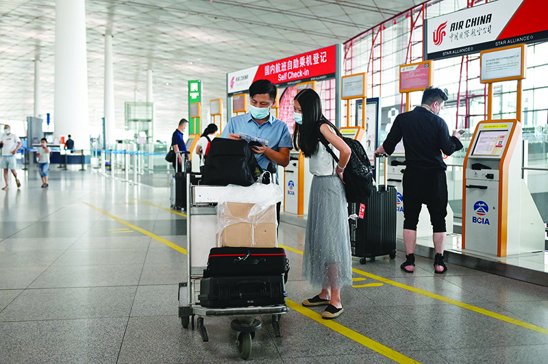 BEIJING: Travellers wearing face masks inspect their tickets after conducting self check-in procedures at the Beijing International Airport yesterday. Beijing’s airports cancelled more than 1,200 flights and schools in the Chinese capital were closed again as authorities rushed to contain a new coronavirus outbreak linked to a wholesale food market. — AFP