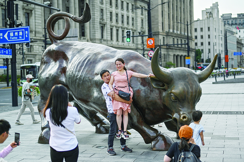 SHANGHAI: A couple pose for their friends next to The Bund Bull on the Bund along the Huangpu River in Shanghai. — AFP