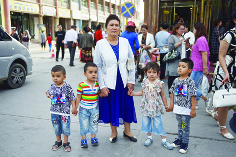 (FILES) This file photo taken on June 4, 2019 shows a Uighur woman waiting with children on a street in Kashgar in China's northwest Xinjiang region. - Chinese authorities are carrying out forced sterilisations of women in an apparent campaign to curb the growth of ethnic minority populations in the western Xinjiang region, according to research published on June 29, 2020. (Photo by GREG BAKER / AFP)