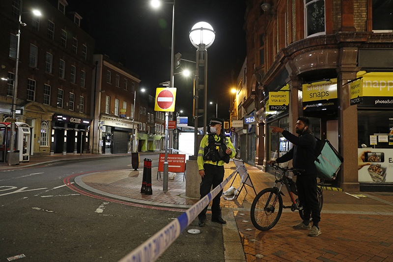 READING: A delivery rider talks to a police officer securing a police cordon in central Reading on Saturday following a stabbing incident at Forbury Gardens park. — AFP