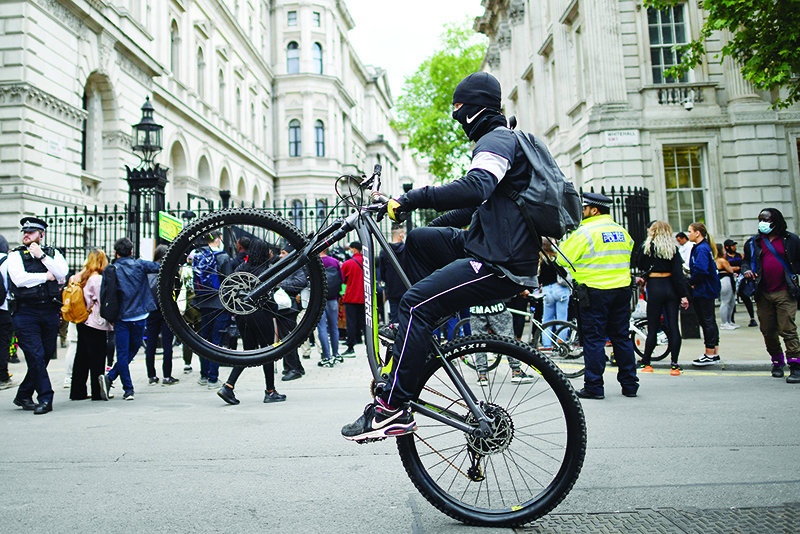 LONDON: A man pulls a wheelie on a bike as he cycles past demonstrators during a Stand up to Racism protest outside of Downing Street on Whitehall, central London in solidarity with the Black Lives Matter movement in the wake of the killing of George Floyd, an unarmed black man who died after a police officer knelt on his neck in Minneapolis, US. — AFP