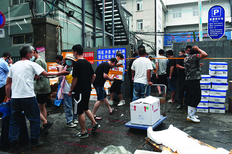 BEIJING: People carry goods out of a side entrance of the Jingshen seafood market yesterday. The market was closed for disinfection and investigation on Friday after it was found that a newly-identified coronavirus patient had visited it. — AFP