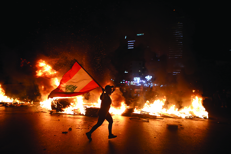 JAL EL DIB, Lebanon: A protester holding the Lebanese flag runs as protesters block the Jounieh Tripoli highway with flaming tyres during a demonstration against dire economic conditions northeast of Beirut late on June 11, 2020. – AFP