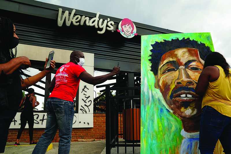 ATLANTA: People use their cellphones to document a muralist painting the face of Rayshard Brooks outside a burned Wendy’s restaurant on Sunday. —  AFP