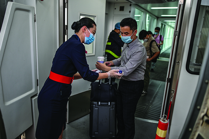 WUHAN, China: This photo taken on May 29, 2020 shows a flight attendant wearing a facemask as she checks the body temperature of boarding passengers next to the door of the plane at Tianhe Airport. –—AFP
