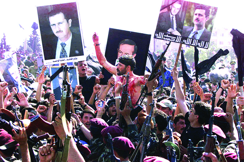 DAMASCUS: In this file photo, Syrian presidential guards, waving pictures of President Hafez Al-Assad and his son, heir apparent Bashar, pay their last respects to their late president in the capital Damascus. — AFP