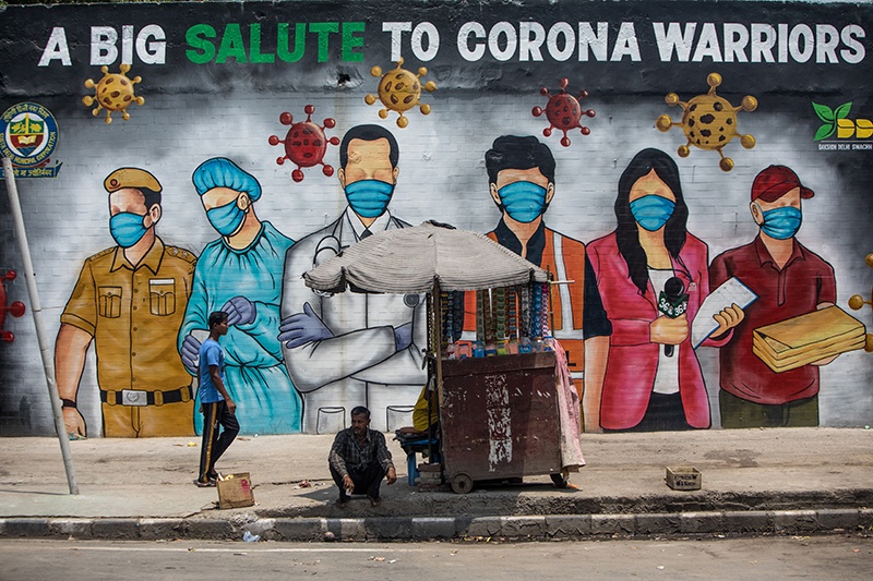 NEW DELHI: A man rests in the shade of a stall (R) while another walks past a mural showing images of frontline workers after the government eased a nationwide lockdown imposed as a preventive measure against the COVID-19 coronavirus in New Delhi yesterday. — AFP