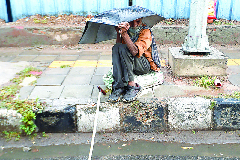 NEW DELHI: A man sits with his umbrella on a road side during a rainy day in New Delhi yesterday. —AFP