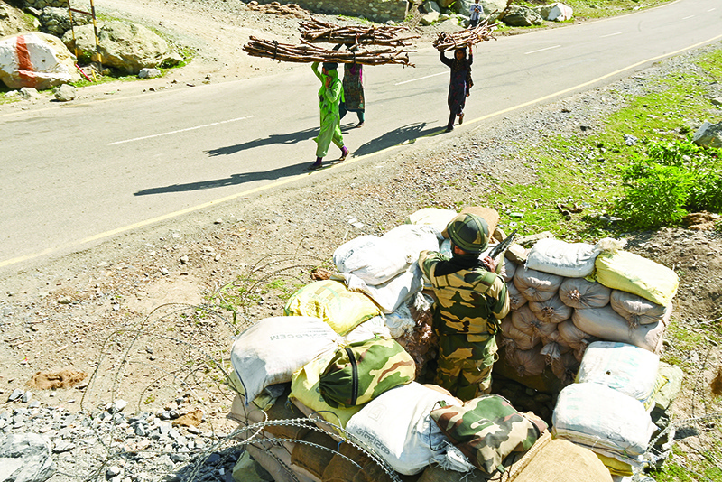 GAGANGIR: An Indian Border Security Force (BSF) soldier guards a highway leading towards Leh, bordering China, as villagers carry firewood in Gagangir. – AFP