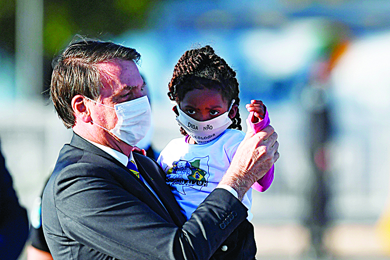 BRASILIA: Brazilian President Jair Bolsonaro holds a girl in his arms, both wearing face masks, during the flag-raising ceremony before a ministerial meeting at the Alvorada Palace in Brasilia, amid the new coronavirus pandemic. —AFP