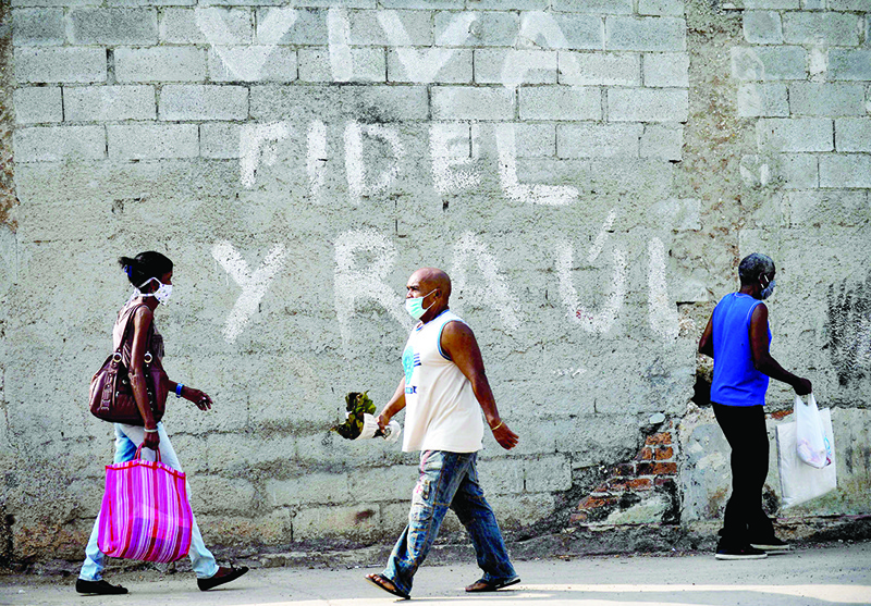 HAVANA: Afro-Cubans wear face masks as a preventive measure against the spread of the novel coronavirus, COVID-19, as they walk past a graffiti reading ‘Long Live Fidel and Raul (Castro)’ in Havana. —  AFP