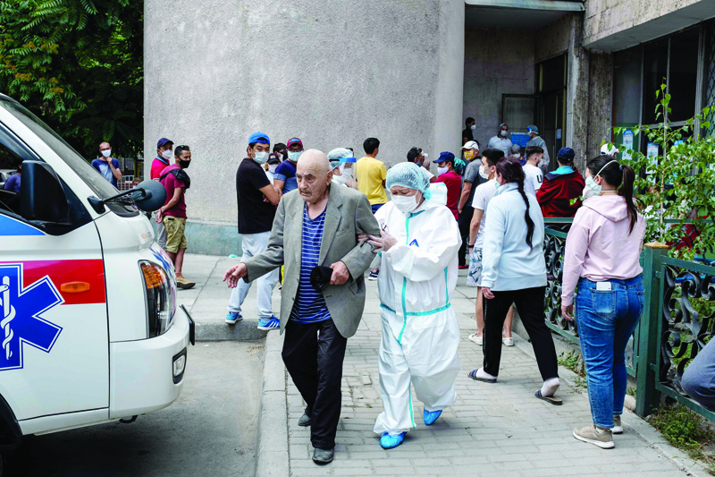 A medical person assists an elderly man on the way to an ambulance in front of a medical facility for people suffering from coronavirus disease and pneumonia in Bishkek on July 5, 2020. (Photo by DANIL USMANOV / AFP)