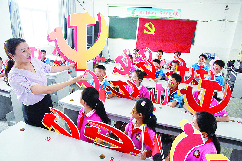 LIANYUNGANG, China: A teacher and her students pose with Communist Party emblems during a class about the history of the Communist Party at a school in China’s eastern Jiangsu province on June 28, 2020. —AFP