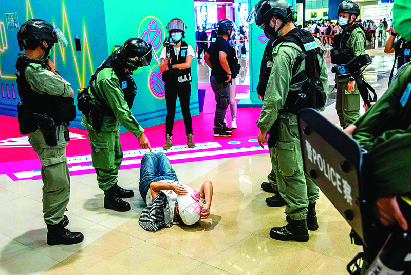 HONG KONG: A riot police officer (2nd left) points at a woman (center) laying down after being searched during a demonstration in a mall in Hong Kong in response to a new national security law. — AFP