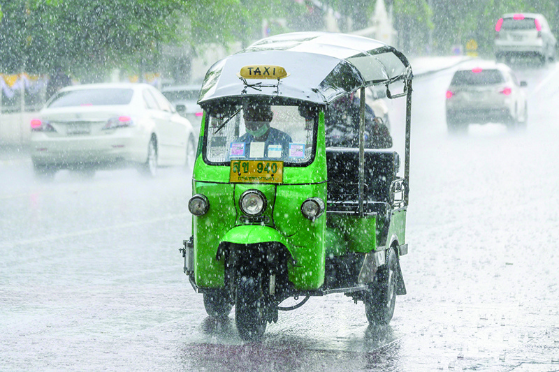 BANGKOK: A traditional Thai tuk tuk drives under a heavy downpour on a street in Bangkok. — AFP
