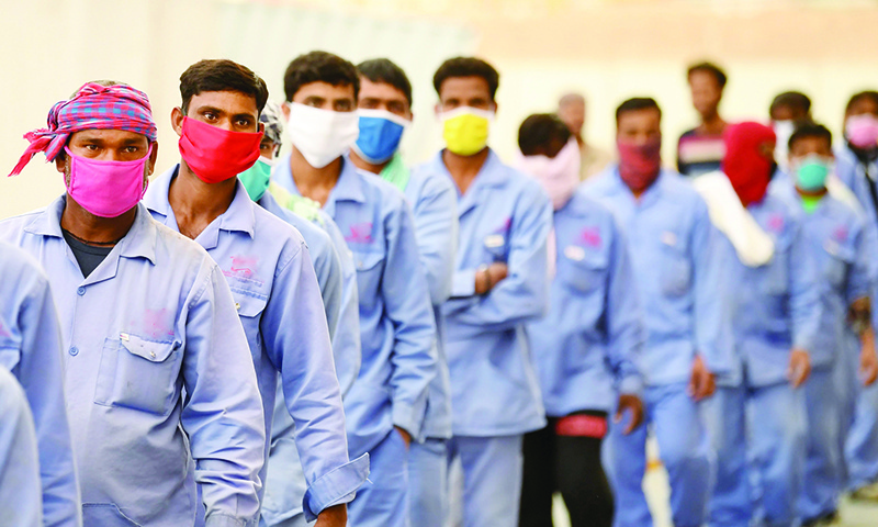 DUBAI: In this file photo, foreign workers wearing scarves to protect their faces, stand in line to board a bus transporting them to their workplace, during the novel coronavirus pandemic crisis, in Dubai. —AFP