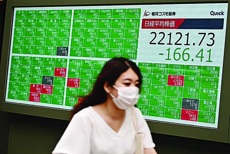TOKYO: A woman wearing a face mask rides her bike in front of an electric quotation board showing numbers of the Nikkei 225 index in Tokyo yesterday. —AFP