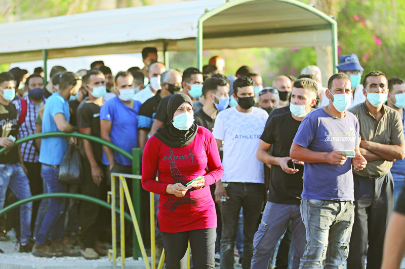 Palestinian workers wearing masks against Covid-19 lineup for a security check at the entrance to Israel's Mishor Adumim industrial zone nearby the Maale Adumim settlement in the West Bank east of Jerusalem, on July 1, 2020. - The government of Israeli Prime Minister Benjamin Netanyahu has said it could begin the process to annex Jewish settlements in the West Bank as well as the strategic Jordan Valley from today. The plan -- endorsed by Washington -- would see the creation of a Palestinian state, but on reduced territory, and without Palestinians' core demand of a capital in east Jerusalem. (Photo by MENAHEM KAHANA / AFP)