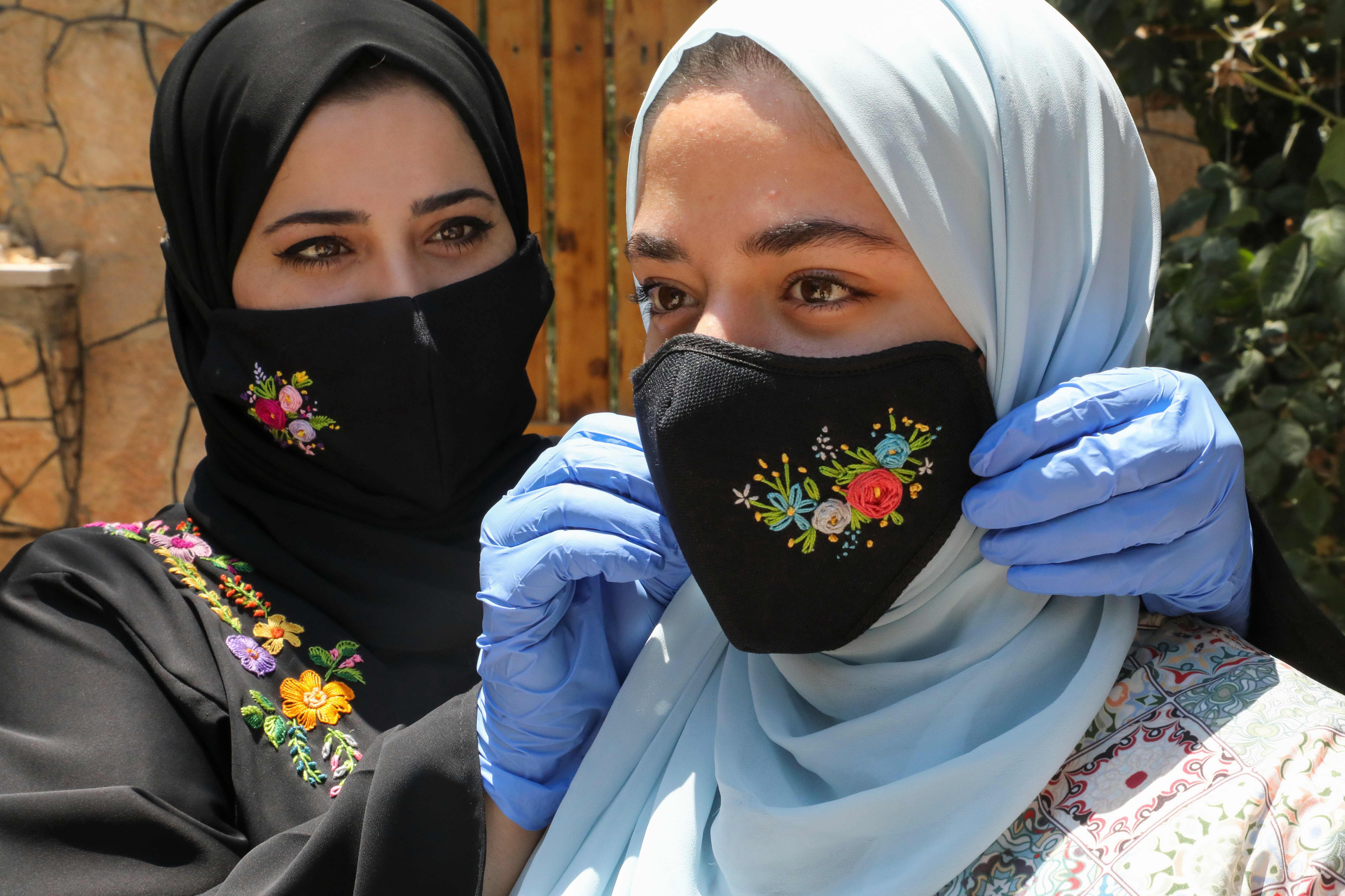 Palestinian Waad Manasra adjusts one of her hand-embroidered protective masks, sold also online, on a customer's face at her home in the village of Bani Naim, east of the West Bank city of Hebron, on July 6, 2020, amid the COVID-19 pandemic. (Photo by HAZEM BADER / AFP)